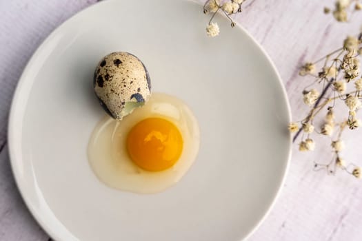 Fresh broken quail egg, yolk and white on a white plate. Bright festive background. Close-up. Healthy eating. top view