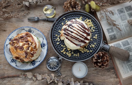 Two Homemade Soft Chocolate Buns, Cinnamon roll topped with rich cream cheese frosting and Caramel Pecanbon topped with caramel frosting and pecans served with Metal fork on old rustic wooden table. The concept of delicious dessert, Top view, Selective focus.