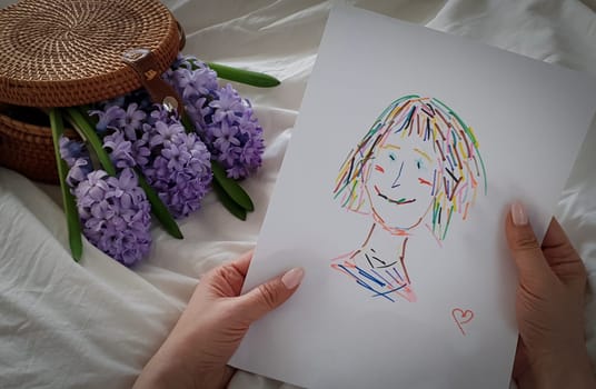 Mom holds a drawing of a child in her hands. Children's drawing. Memories of my mother.