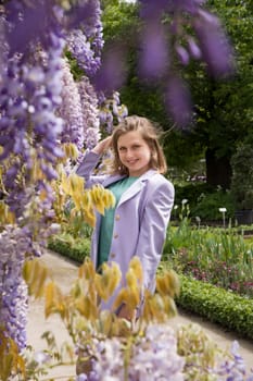 A young woman in a lilac jacket poses near the flowering wisteria in the Botanical Garden. High quality photo