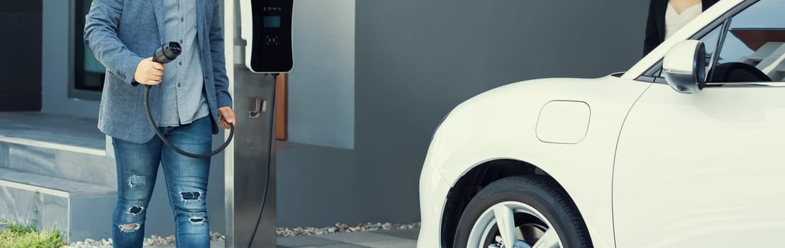 Closeup progressive asian man install cable plug to his electric car with home charging station. Concept of the use of electric vehicles in a progressive lifestyle contributes to clean environment.