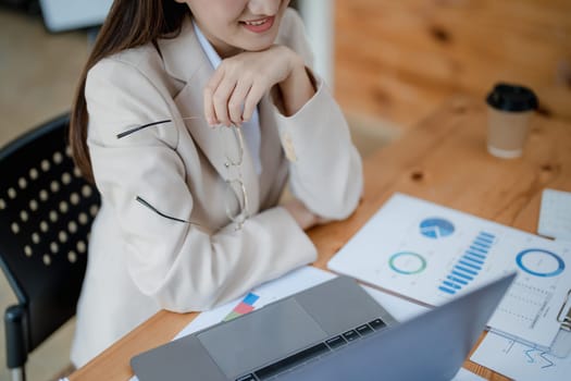 Portrait of a woman business owner showing a happy smiling face as he has successfully invested her business using computers and financial budget documents at work.