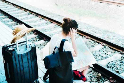 summer, relax, vacation, travel, portrait of a cute Asian girl looking at a map to plan a trip while waiting at the train station