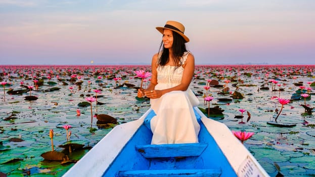 Asian women in a boat at the Beautiful Red Lotus Sea Kumphawapi is full of pink flowers in Udon Thani in northern Thailand. Flora of Southeast Asia.