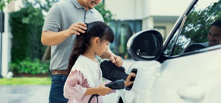 Progressive father and daughter returned from school in electric vehicle that is being charged at home. Electric vehicle driven by renewable clean energy. Home charging station concept for environment