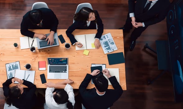 Top view manager or office worker give presentation in harmony conference room to business colleague, BI data dashboard on screen and pile of financial analyzed data reports on meeting table.