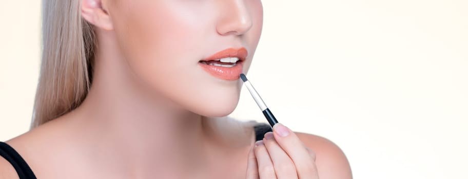 Closeup personable young woman with flawless healthy skin and natural makeup putting fashion glossy lipstick on her lip with lip brush in isolated background. Facial cosmetic makeup in process.