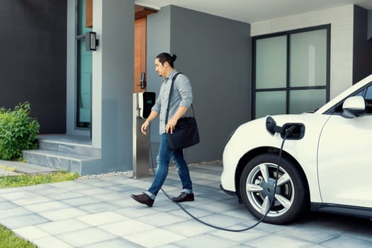 Progressive asian man and electric car with home charging station. Concept of the use of electric vehicles in a progressive lifestyle contributes to a clean and healthy environment.