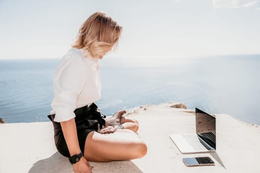 Happy girl doing yoga with laptop working at the beach. beautiful and calm business woman sitting with a laptop in a summer cafe in the lotus position meditating and relaxing. freelance girl remote work beach paradise