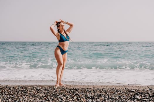 Beach vacation. Hot beautiful woman in sunhat and bikini standing with her arms raised to her head enjoying looking view of beach ocean on hot summer day.