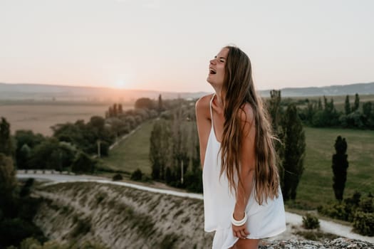 Romantic beautiful bride in white dress posing with sea and mountains in background. Stylish bride standing back on beautiful landscape of sea and mountains on sunset