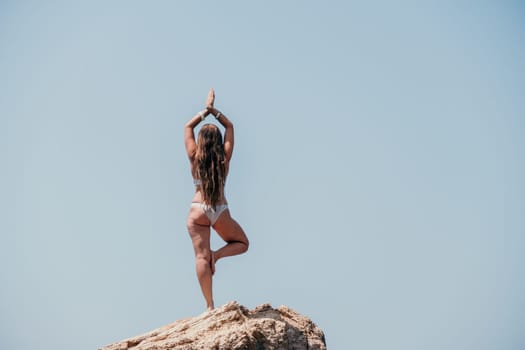 Woman meditating in yoga pose silhouette at the ocean, beach and rock mountains. Motivation and inspirational fit and exercising. Healthy lifestyle outdoors in nature, fitness concept.