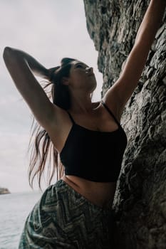 A girl climbs a rock. The athlete trains in nature. Woman overcomes difficult climbing route. Extreme hobby. Tourist woman rock climber hiking on mountains rocks over beautiful sea coast