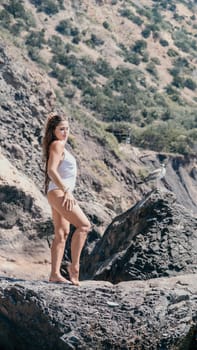 Woman travel sea. Young Happy woman in a long red dress posing on a beach near the sea on background of volcanic rocks, like in Iceland, sharing travel adventure journey