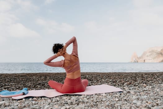 Middle aged well looking woman with black hair doing Pilates with the ring on the yoga mat near the sea on the pebble beach. Female fitness yoga concept. Healthy lifestyle, harmony and meditation.