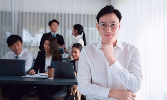 Portrait of focus young successful confident male manager, executive wearing business wear in harmony office arm crossed with blurred meeting background of colleagues, office worker.