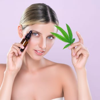 Alluring portrait of beautiful woman in pink isolated background holding green leaf with marijuan extracted bottle for skincare treatment product. Cannabis CBD oil for cosmetology and beauty concept.