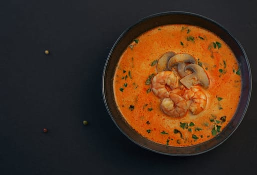 Tom Yum kung Spicy Thai soup with shrimp in a black bowl on a dark background,