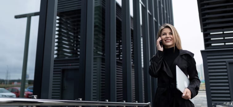 wide horizontal photo of a confident business woman in front of an office building.