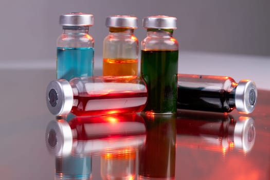 Collection of drug vials with colored solution. Vaccine bottles on reflective surface.