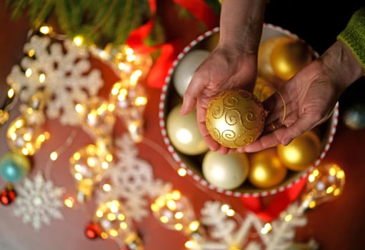 Female hands holding Merry Christmas toy above gift box on red decorated festive background, top view.