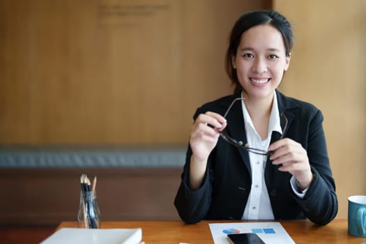 Portrait of a young Asian woman showing a smiling face using a computer and financial statements.