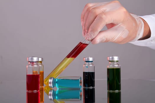 Doctors hand holding test tube with blood. Drug vials with colored solution.