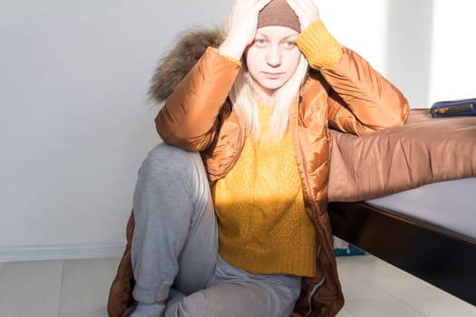 A girl in a yellow sweater and jacket holds her head with her hands from big problems and stress. The concept of the economic crisis and large utility bills in homes