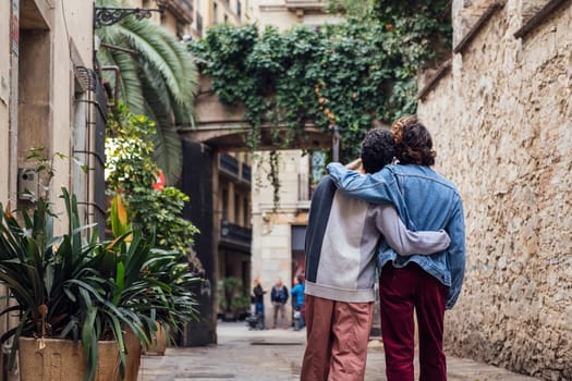 rear view of a gay male couple walking embraced along a beautiful ancient street decorated with plants, concept of leisure and love between people of the same sex