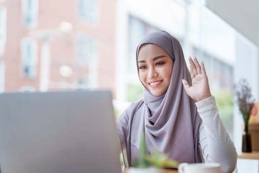 Beautiful Muslim woman using computer to greet attendees via video conference.