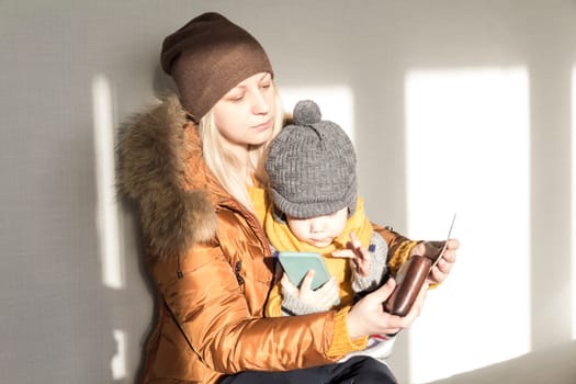 A mother with a small child in her arms is warmly dressed in outerwear, counting money in her purse. The concept of the economic crisis and large utility bills in homes