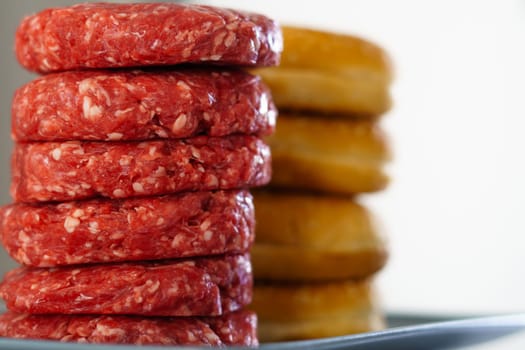 stack of raw beef burgers with their buns on a mirrored white plate