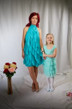 Amazing pretty mother and daughter having fun with flowers in 8 March or in Mother's day. Red haired mom and small little blonde girl having lovely free time on white background in studio