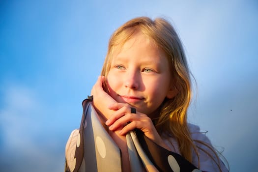 Portrait of pretty blonde girl and blue sky on background in a sunny summer day. Portrait of teenage child in summer or spring outdoors