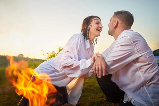 Happy Couple relaxin, having fun and hugs with fire in camping on nature near water of river or lake in summer sunny evening in sunset. Family or lovers have date and rest outdoor. Concept of love