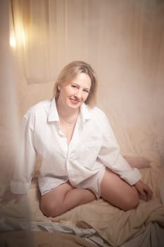 Portrait of sexual body positive adult lady woman in intimate in tender space indoors in a bedroom. Plump girl poses in black underwear and white shirt during boudoir style photo shoot