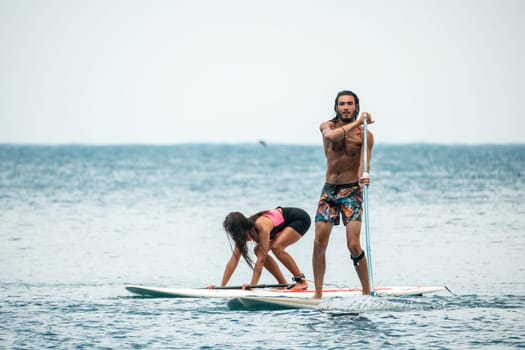 Sea woman and man on sup. Silhouette of happy young woman and man, surfing on SUP board, confident paddling through water surface. Idyllic sunset. Active lifestyle at sea or river