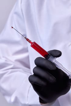 Close up doctors hand with black glove holding a syringe.