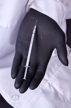 Hand in black glove holding cosmetic syringe. Vertical shot close up.