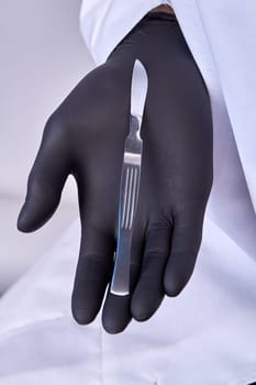 Hand in a surgical glove holding a scalpel. Vertical shot close up.