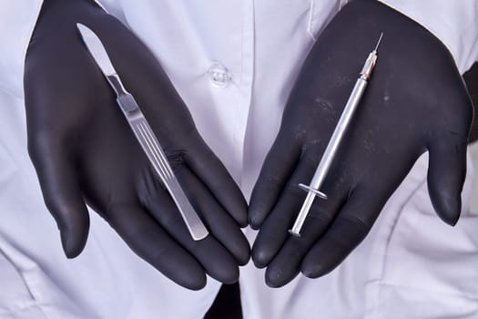 Close up doctors hands in gloves holding tools for cosmetic surgery. Scalpel and syringe.