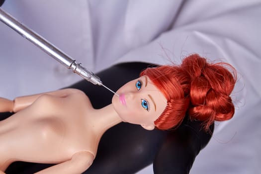 Cosmetic syringe injection in a plastic ginger dolls lips. Concept of surgery.