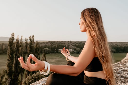 Well looking middle aged woman with long hair, fitness instructor in leggings and tops doing stretching and pilates on the rock near forest. Female fitness yoga routine concept. Healthy lifestyle.