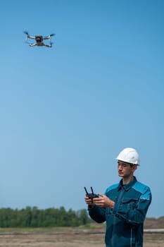 A man in a helmet and overalls controls a drone at a construction site. The builder carries out technical oversight