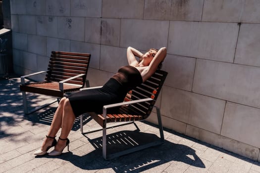 Portrait of a woman on the street. An attractive woman in a black dress is sitting on a bench outside