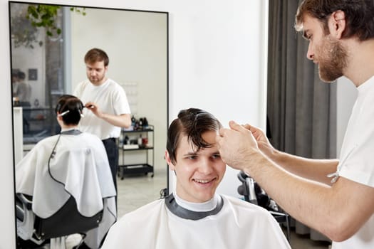 Professional barber during work with man client in barber shop.