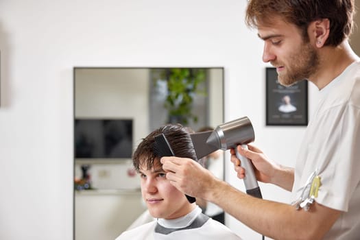 Professional hairdresser using hair dryer and comb in barber shop. Haircut in the barbershop.