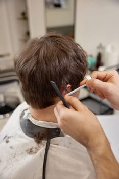 hairdresser does haircut for caucasian man in barber shop. close-up