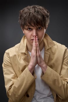 young man in coat holding hands in pray on black background.