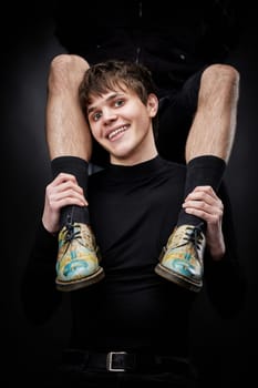 young handsome guy hugs male legs in bright shoes on black background. fashion